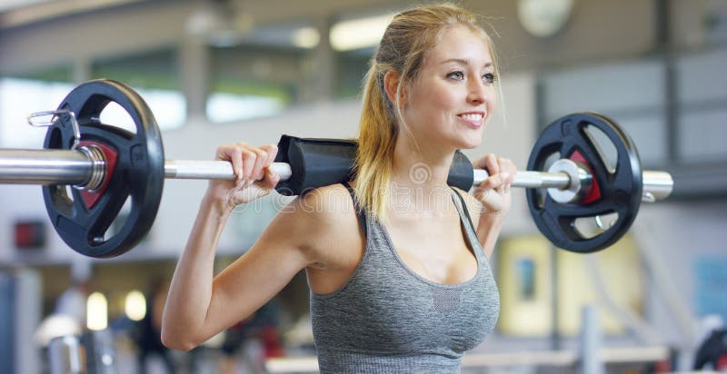 Jeune belle fille dans le gymnase faisant des exercices sur la posture accroupie avec un barbell, améliorant les muscles des fess photographie stock libre de droits Jeune belle fille dans le gymnase faisant des exercices sur la posture accroupie avec un barbell, améliorant les muscles des fess photographie stock libre de droits