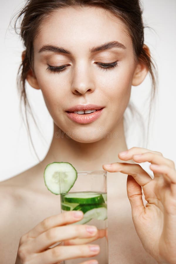 Jeune belle fille nue avec la peau propre parfaite souriant tenant le verre de l'eau avec des tranches de concombre au-dessus de photographie stock libre de droits Jeune belle fille nue avec la peau propre parfaite souriant tenant le verre de l'eau avec des tranches de concombre au-dessus de photographie stock libre de droits