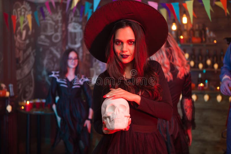 Young beautiful witch doing dark magic on a human skull for halloween celebration. Witch halloween costume. Young beautiful witch doing dark magic on a human skull for halloween celebration. Witch halloween costume.