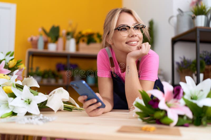 Jeune blonde fleuriste utilisant smartphone se penchant sur la table à la boutique de fleurs photo libre de droits