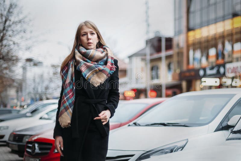 Jeune blonde heureuse de femme dans un manteau noir et des promenades d'écharpe par la ville Se réunir de attente image libre de droits Jeune blonde heureuse de femme dans un manteau noir et des promenades d'écharpe par la ville Se réunir de attente image libre de droits