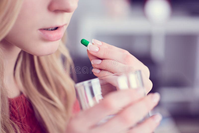 Jeune blonde mignonne prenant une pilule avec un verre de l'eau à la maison images libres de droits Jeune blonde mignonne prenant une pilule avec un verre de l'eau à la maison images libres de droits