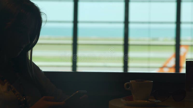 Jeune café potable de sourire de femme en café d'aéroport, message de dactylographie sur le téléphone portable clips vidéos