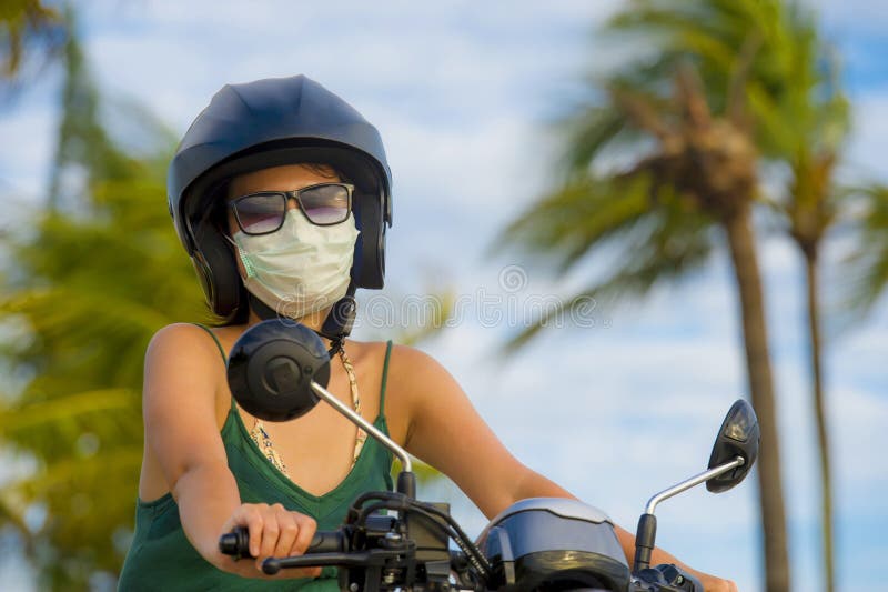 Young happy and pretty Asian Chinese woman riding scooter wearing safety motorcycle helmet and protective face mask in motorbike safe ride and traffic air contamination and pollution concept. Young happy and pretty Asian Chinese woman riding scooter wearing safety motorcycle helmet and protective face mask in motorbike safe ride and traffic air contamination and pollution concept