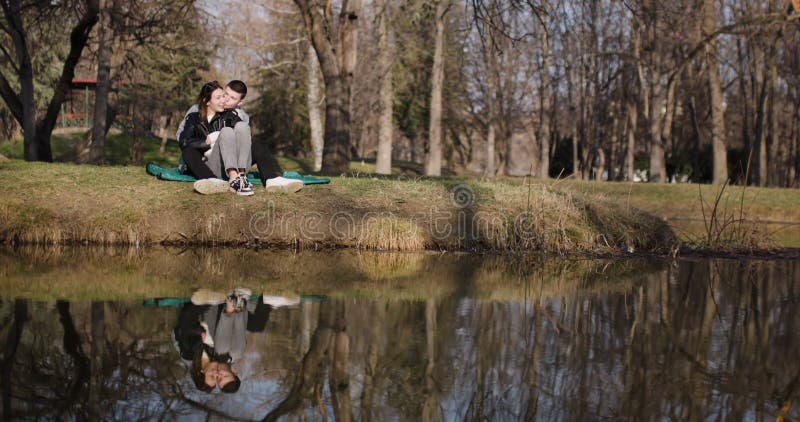 Jeune couple capture Selfies et profite d'un après-midi relaxant au bord du lac dans un parc panoramique banque de vidéos