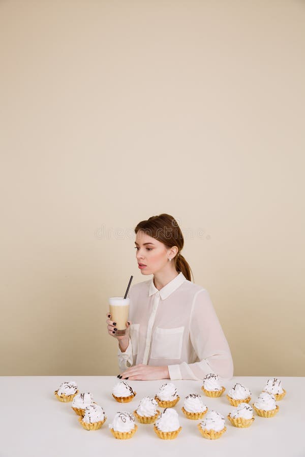 Jeune dame concentrée posant près des petits gâteaux tenant le café photo stock