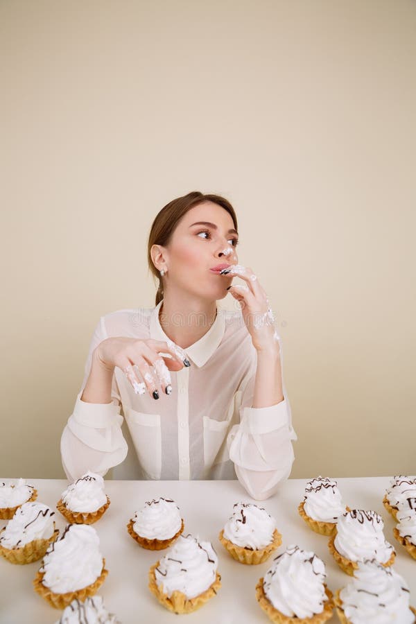 Jeune dame concentrée posant tout en mangeant des petits gâteaux photographie stock libre de droits