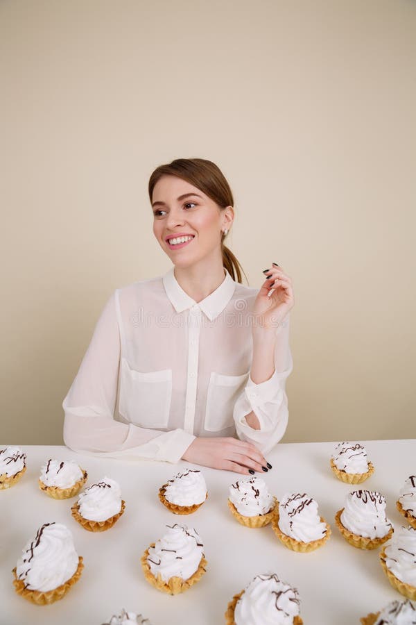 Jeune dame de sourire posant tout en se reposant près du petit gâteau sur la table photographie stock