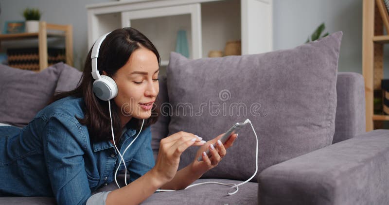 Jeune dame joyeuse touchant l'écran de smartphone écoutant la musique dans des écouteurs banque de vidéos