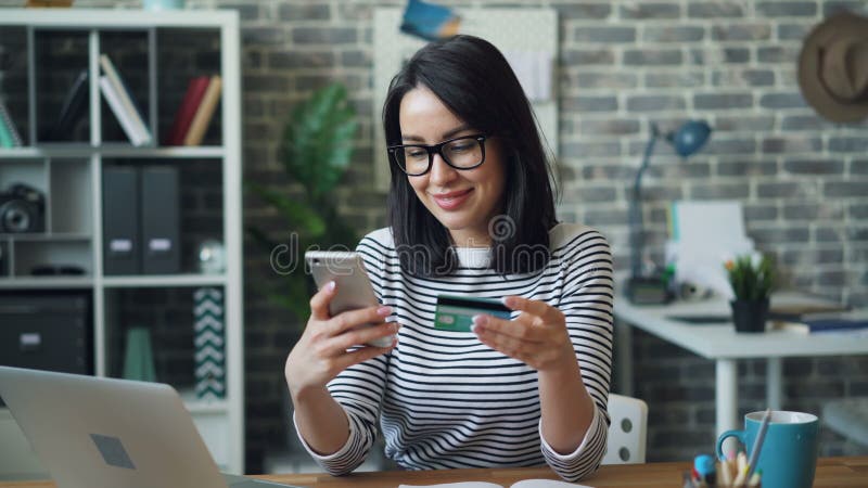 Jeune dame payant en ligne avec la carte de crédit utilisant le smartphone dans le lieu de travail banque de vidéos