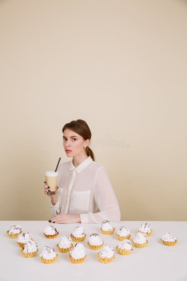 Jeune dame sérieuse posant près des petits gâteaux tenant le café image stock