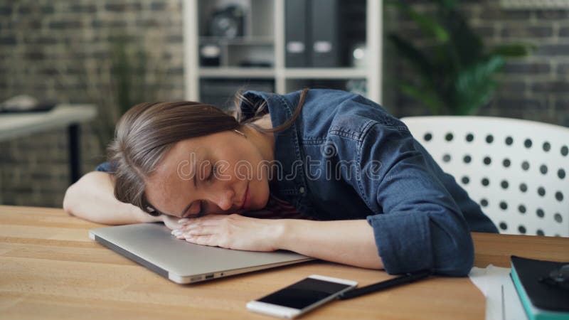 Jeune dame épuisée dormant sur l'ordinateur portable au travail se reposant après dure journée banque de vidéos