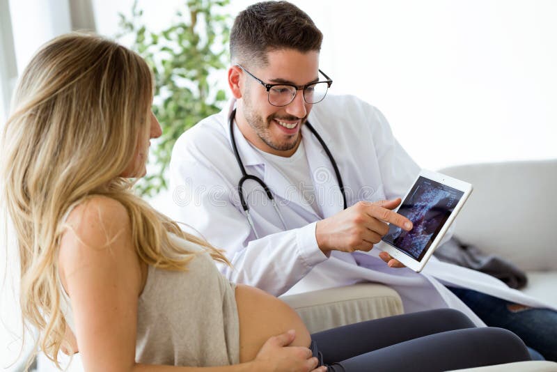 Jeune docteur masculin de gynécologue montrant au bébé de balayage d'ultrason de femme enceinte avec le comprimé numérique photo libre de droits Jeune docteur masculin de gynécologue montrant au bébé de balayage d'ultrason de femme enceinte avec le comprimé numérique photo libre de droits