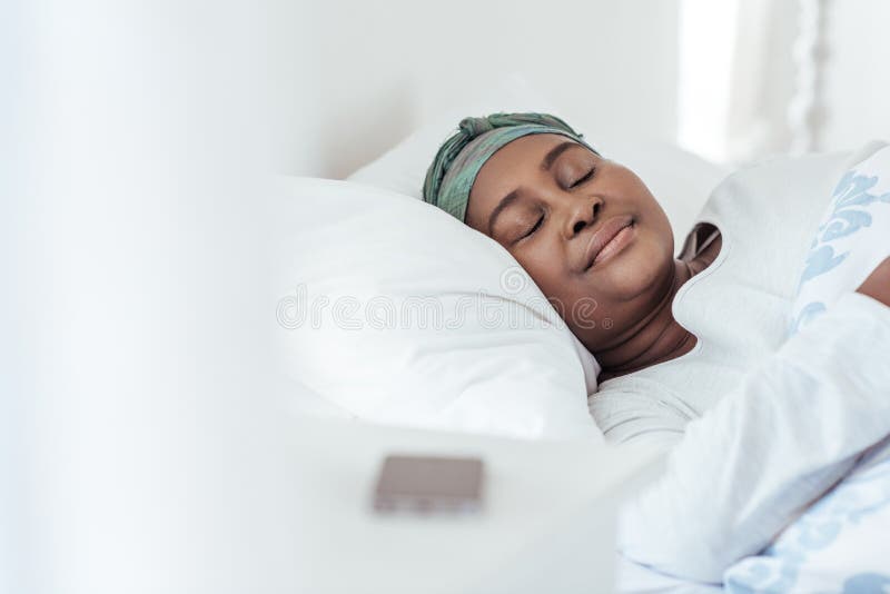 Young African woman wearing a headscarf fast asleep under the duvet of her bed at home in the early morning. Young African woman wearing a headscarf fast asleep under the duvet of her bed at home in the early morning