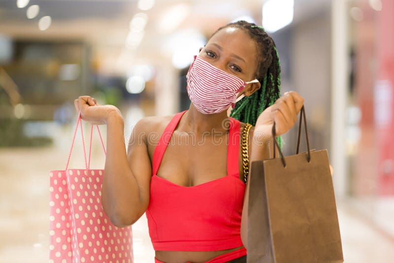 Young African American woman at shopping mall in new normal after covid-19 - happy and beautiful black girl in face mask holding shopping bags enjoying at beauty fashion store. Young African American woman at shopping mall in new normal after covid-19 - happy and beautiful black girl in face mask holding shopping bags enjoying at beauty fashion store