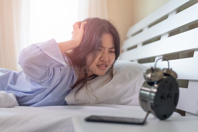 Jeune femme asiatique choquée comme elle se réveillant tard dans le matin, jeune fille s'étendant dans le lit photos libres de droits Jeune femme asiatique choquée comme elle se réveillant tard dans le matin, jeune fille s'étendant dans le lit photos libres de droits