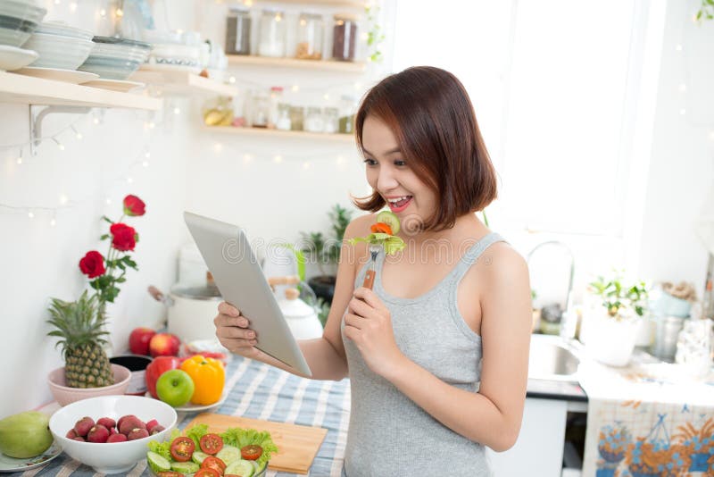 Jeune femme asiatique mangeant de la nourriture saine et employant un calcul de comprimé photo stock Jeune femme asiatique mangeant de la nourriture saine et employant un calcul de comprimé photo stock