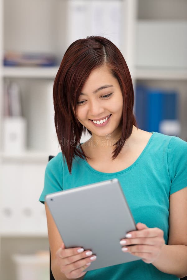 Jeune femme asiatique souriant comme elle lit son comprimé images libres de droits