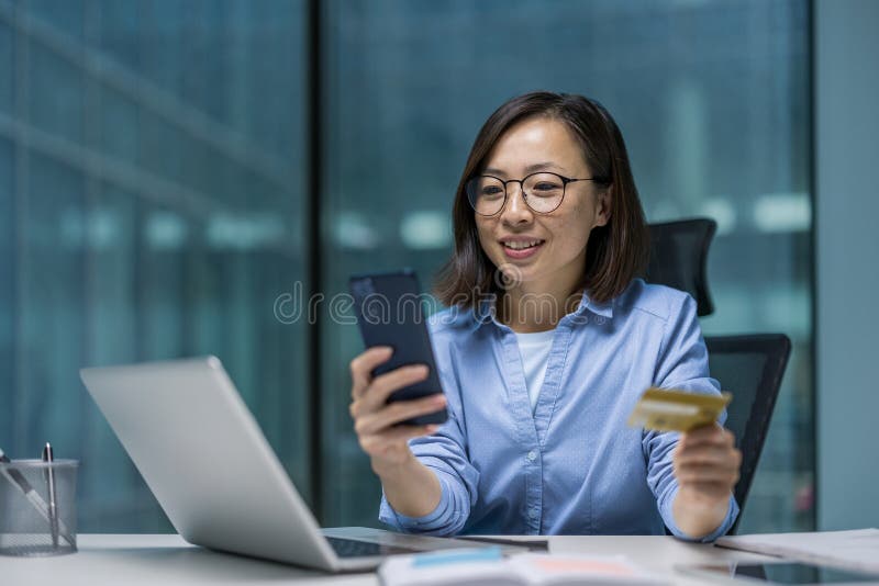 Jeune femme asiatique à succès au travail dans le bureau avec téléphone et carte de crédit bancaire mains. Femme d'affaires choisi image stock