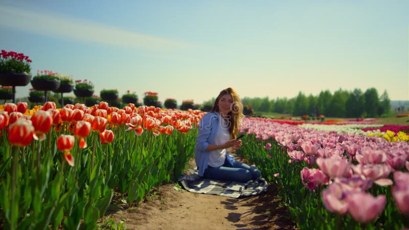 Jeune femme assise dans un jardin fleuri avec un téléphone portable par jour ensoleillé. clips vidéos