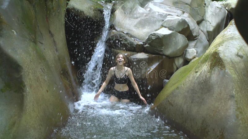 Jeune femme attirante dans le mouvement lent éclaboussant l'eau claire du lac de montagne de la petite cascade dans tropical vert