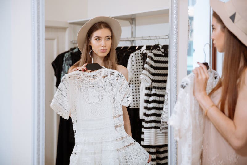 Jeune femme attirante essayant sur la robe devant le miroir photos stock Jeune femme attirante essayant sur la robe devant le miroir photos stock