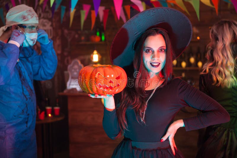 Attractive young women dressed up like a witch for halloween posing in front of the camera. Creepy doctor in the background. Attractive young women dressed up like a witch for halloween posing in front of the camera. Creepy doctor in the background.