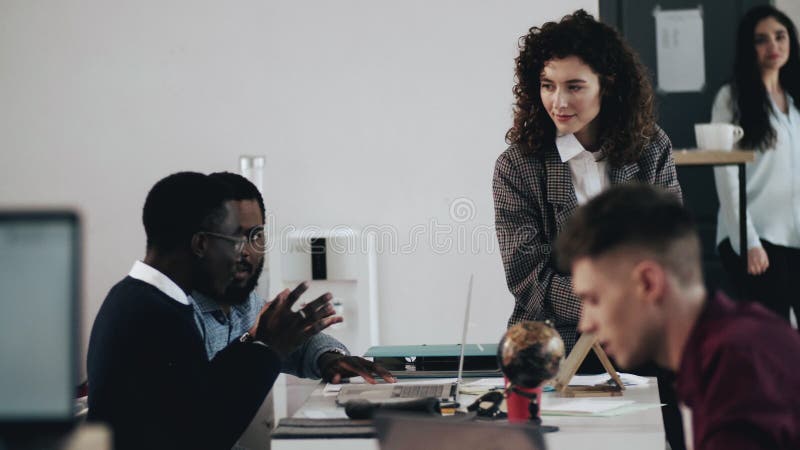 Jeune femme attirante professionnelle heureuse de mentor des affaires enseignant deux directeurs masculins noirs à la table moder banque de vidéos