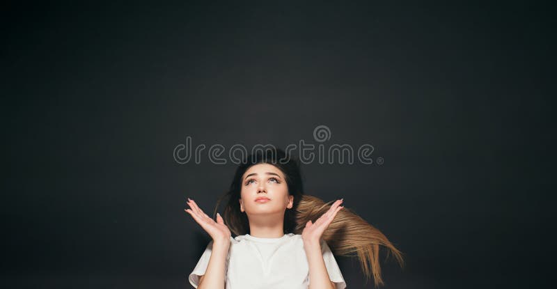 Jeune femme aux cheveux longs regardant d'un ton de prière les bras répandus à la hausse pour l'étudiant de côtés sur le fond noir images stock