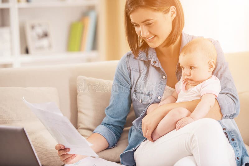 Jeune femme avec le bébé travaillant à la maison avec l'ordinateur portable photo stock Jeune femme avec le bébé travaillant à la maison avec l'ordinateur portable photo stock