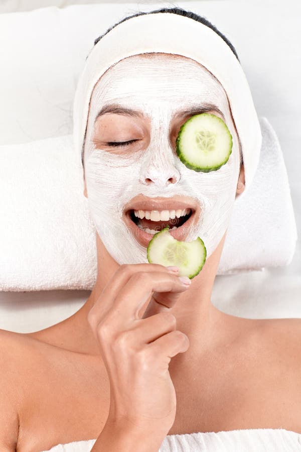 Young woman having face mask and cucumber on eyes, biting cucumber, smiling. Young woman having face mask and cucumber on eyes, biting cucumber, smiling.