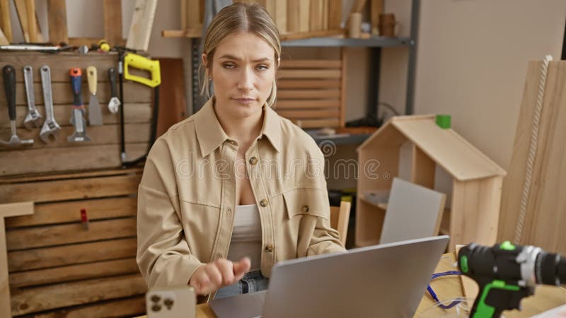 Jeune femme blonde confiante à l'atelier de menuiserie expression sérieuse alors qu'elle lève le signe stop avec sa main en utilis banque de vidéos