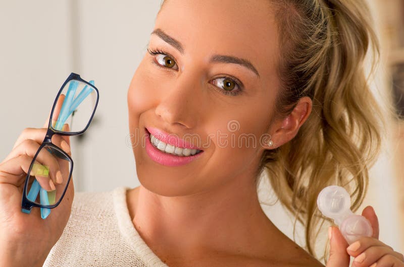 Jeune femme blonde de sourire tenant la caisse de verre de contact en main et tenant dans son autre main par verres bleus sur bro photographie stock Jeune femme blonde de sourire tenant la caisse de verre de contact en main et tenant dans son autre main par verres bleus sur bro photographie stock
