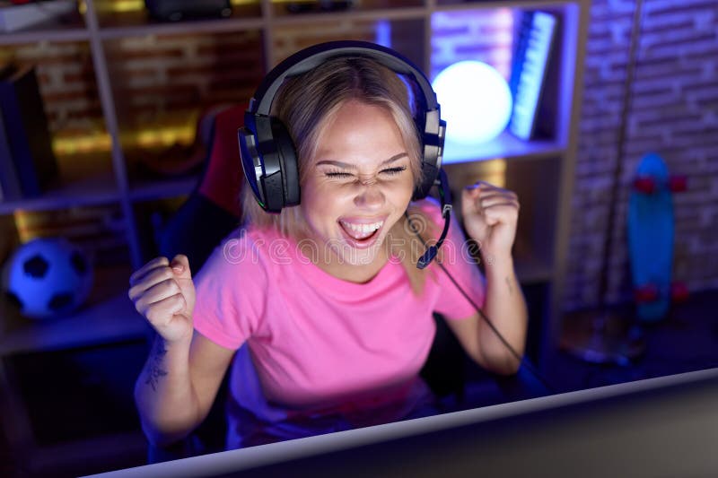 Jeune femme blonde jouer jeu vidéo avec l'expression gagnante à la salle de jeu images stock