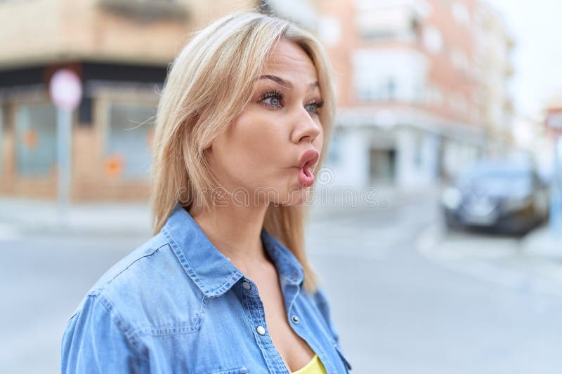 Jeune femme blonde souriante confiante en faisant un geste drôle avec la bouche à la rue photographie stock