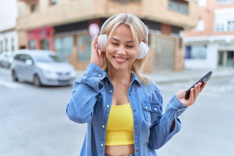 Jeune femme blonde souriante confiante en écoutant de la musique dans la rue photos libres de droits