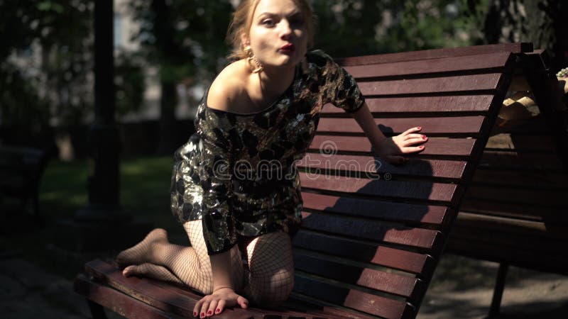 Jeune femme caucasienne pieds nus en tenue de fête sur banc dans le parc debout en regardant loin. portrait de soi assuré clips vidéos
