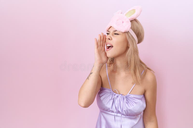 Jeune femme caucasienne portant masque de sommeil et pyjama robe sans idée et confus avec bras ouverts aucune idée et visage doute photographie stock libre de droits