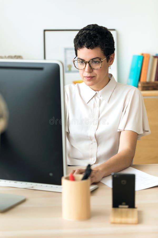 Jeune femme concentrée d'affaires travaillant avec son ordinateur portable dans le bureau image stock Jeune femme concentrée d'affaires travaillant avec son ordinateur portable dans le bureau image stock