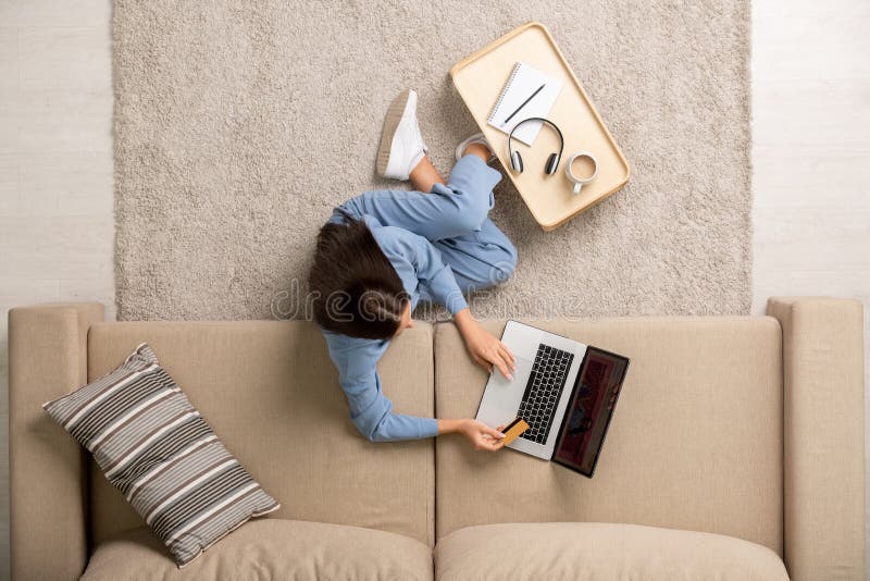 Jeune femme contemporaine en pyjama en utilisant une carte de crédit lors d'achats en ligne image stock