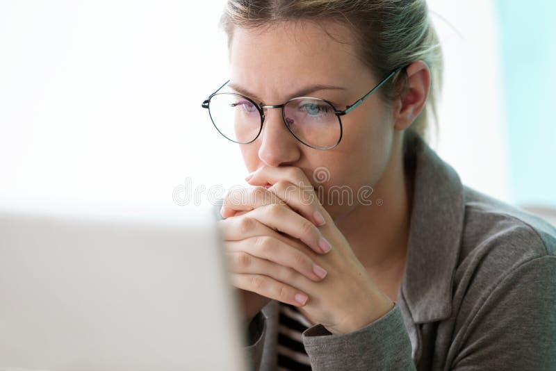 Jeune femme d'affaires de concentré regardant son ordinateur tout en pensant dans le bureau