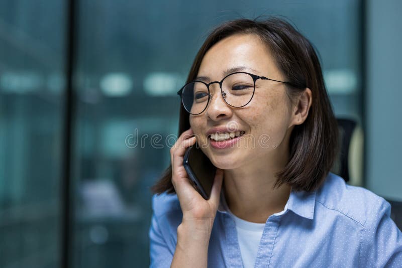 Jeune femme d'affaires prospère parlant au téléphone dans le bureau près. Femme asiatique souriante satisfaite travaillant près du photos libres de droits