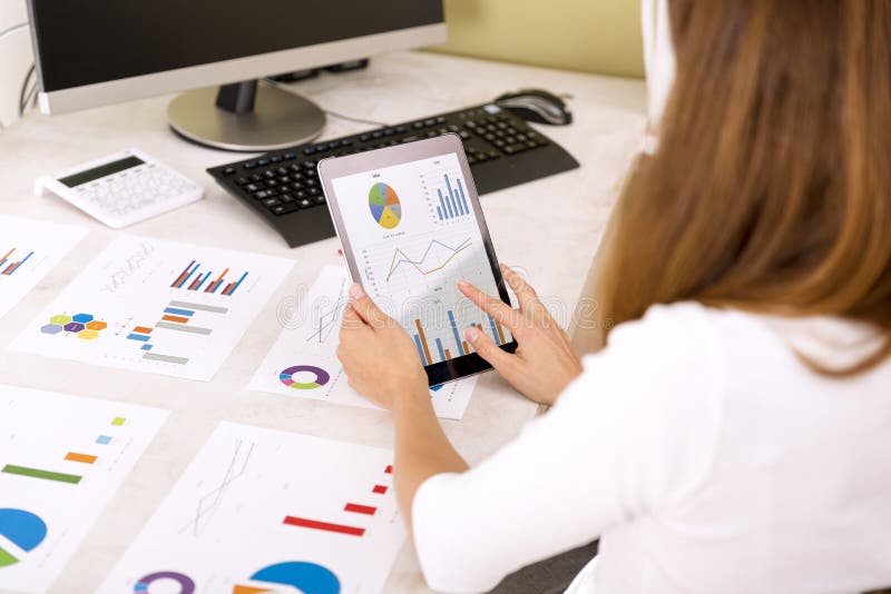 Jeune femme d'affaires réexaminant des résultats de ventes sur le comprimé Graphiques sur la table de bureau photographie stock libre de droits Jeune femme d'affaires réexaminant des résultats de ventes sur le comprimé Graphiques sur la table de bureau photographie stock libre de droits