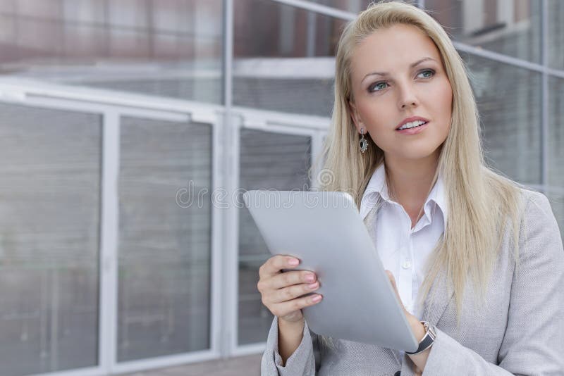 Jeune femme d'affaires réfléchie à l'aide du comprimé numérique tout en regardant loin contre l'immeuble de bureaux image stock Jeune femme d'affaires réfléchie à l'aide du comprimé numérique tout en regardant loin contre l'immeuble de bureaux image stock