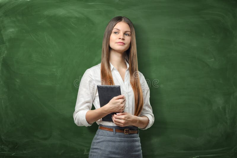 Jeune femme d'affaires tenant son dayplanner et pensant sur le fond vert de tableau images libres de droits Jeune femme d'affaires tenant son dayplanner et pensant sur le fond vert de tableau images libres de droits