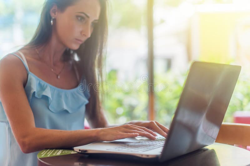 Jeune femme d'affaires travaillant sur son ordinateur portable, dactylographie, se reposant dans un restaurant à côté du matin en photos libres de droits Jeune femme d'affaires travaillant sur son ordinateur portable, dactylographie, se reposant dans un restaurant à côté du matin en photos libres de droits