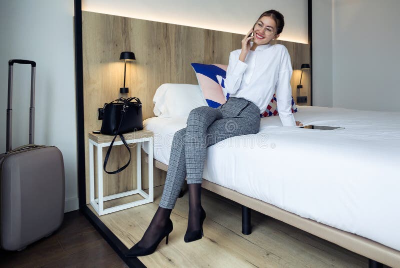Jeune femme d'affaires élégante parlant avec son téléphone de Mobil se reposant sur le lit à la chambre d'hôtel images libres de droits Jeune femme d'affaires élégante parlant avec son téléphone de Mobil se reposant sur le lit à la chambre d'hôtel images libres de droits