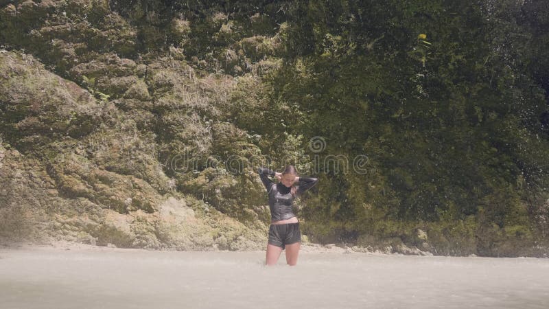 Jeune femme dans des vêtements humides appréciant la cascade débordante dans la position heureuse de femme de forêt tropicale sou