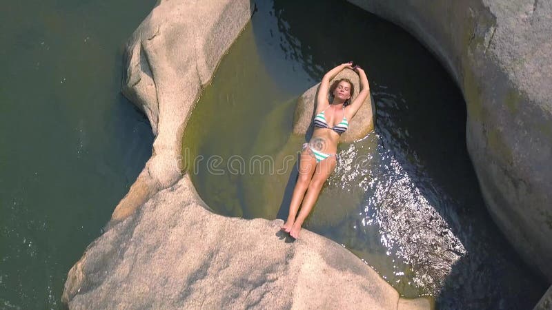Jeune femme dans le maillot de bain se trouvant sur la grande pierre dans la vue de bourdon d'eau de rivière Belle femme détendan clips vidéos