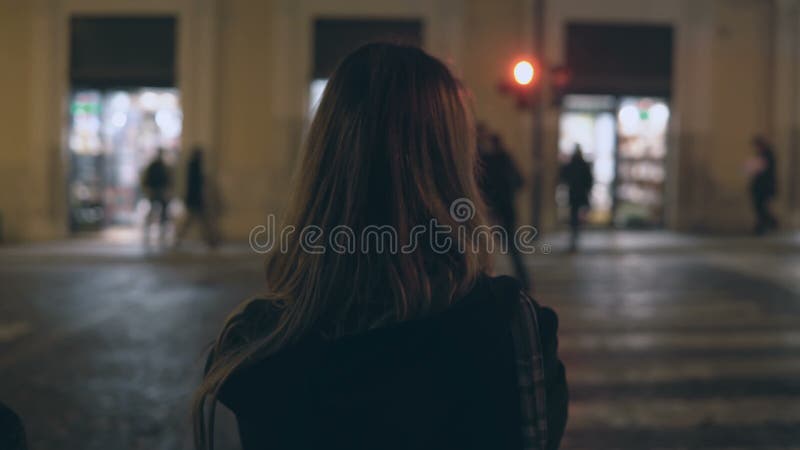 Jeune femme de brune traversant la route du trafic le soir et marchant seul au centre de la ville, par les rues photographie stock Jeune femme de brune traversant la route du trafic le soir et marchant seul au centre de la ville, par les rues photographie stock